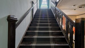 Una imponente escalera con barandilla que lleva a una habitación luminosa con ventana y cortinas.