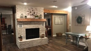 A living room with a stone fireplace, wooden flooring, a dining table, and a couch. - Greer’s Ferry Lake & Little Red River Cabin (Heber Springs)