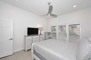 Quarto com cama, televisão em penteadeira, ventilador de teto e guarda-roupa com portas venezianas.