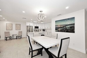 A modern kitchen with white cabinets and stainless steel appliances, a dining area with a marble table, and a large abstract painting on the wall.