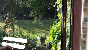 A garden patio with a wooden bench, a pathway leading to a lawn, and various potted plants. - Riverfield Bed and Breakfast (Gorey)