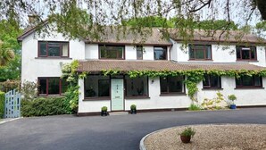 A two-story white building with a tiled roof, multiple windows, and a covered porch with greenery. - Riverfield Bed and Breakfast (Gorey)