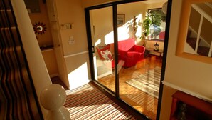 A spacious living area with a red sofa, a glass door leading to a balcony, and a striped carpet. - Riverfield Bed and Breakfast (Gorey)