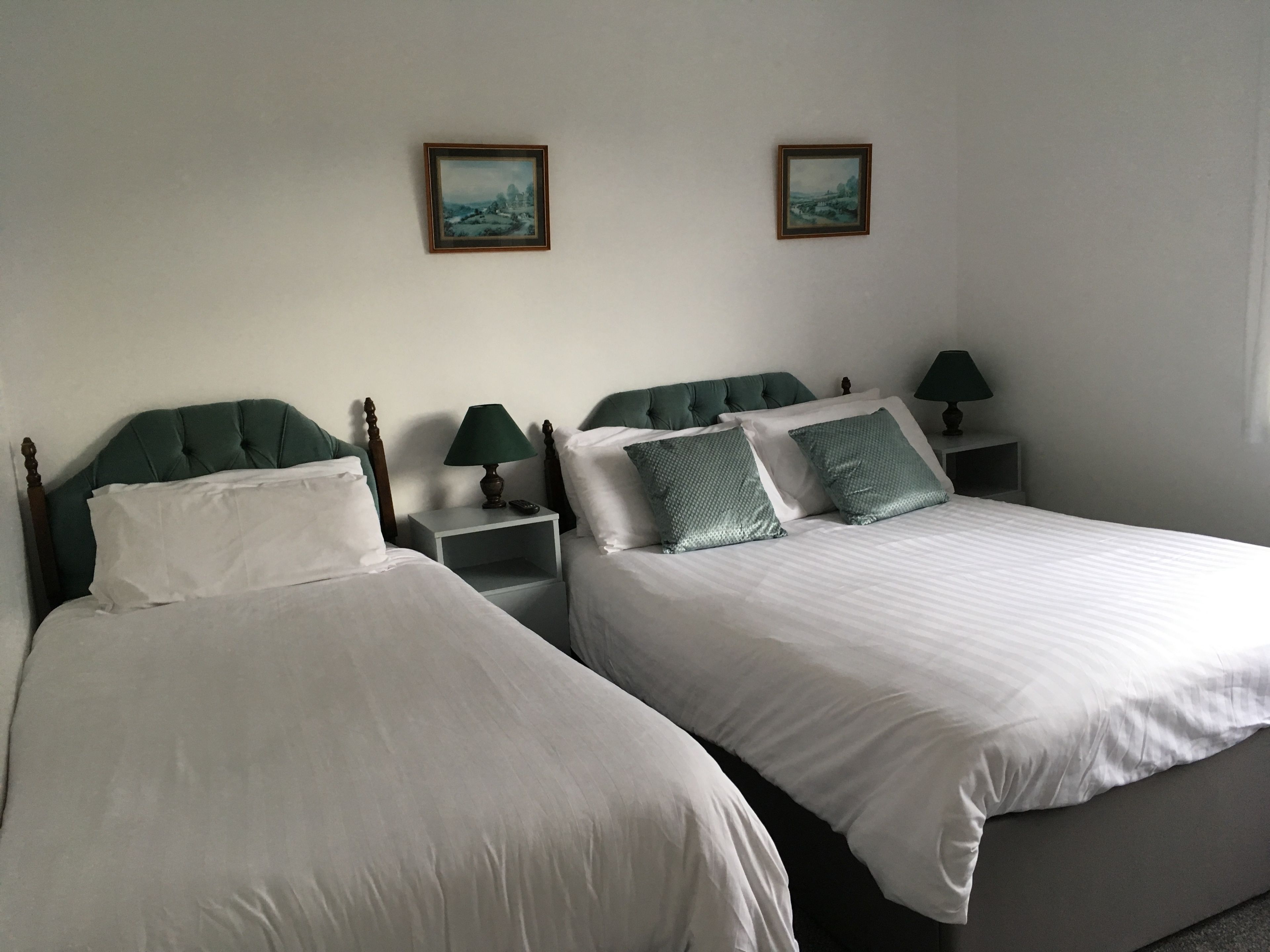 Une chambre d’hôtel avec deux lits, chacun doté d’une tête de lit en bois, de draps blancs et d’un oreiller vert. On y trouve des tables de chevet avec des lampes, ainsi que deux tableaux encadrés accrochés au mur.