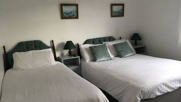 Une chambre d’hôtel avec deux lits, chacun doté d’une tête de lit en bois, de draps blancs et d’un oreiller vert. On y trouve des tables de chevet avec des lampes, ainsi que deux tableaux encadrés accrochés au mur.