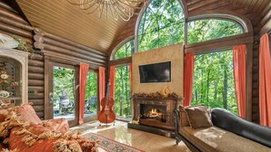 A log cabin interior with a fireplace, large windows, and a cozy seating area. - Romance-Grande Old World-Lux Hot Tub-Kayaks-Private Spa w/ Massage Chair & Sauna (Logan)