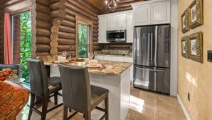 A log cabin interior with a kitchen featuring white cabinets, stainless steel appliances, and a marble countertop. - Romance-Grande Old World-Lux Hot Tub-Kayaks-Private Spa w/ Massage Chair & Sauna (Logan)