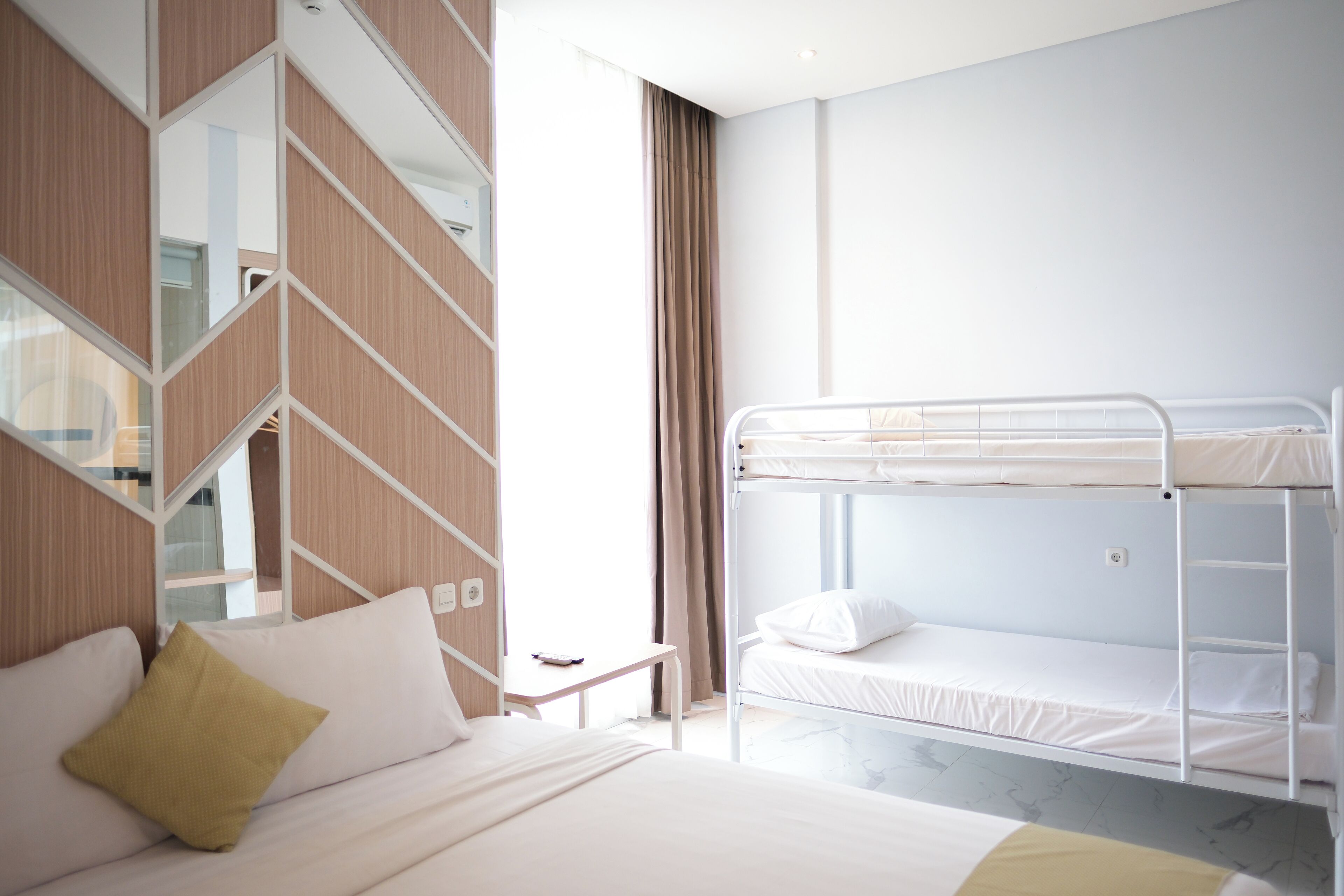 Une chambre d’hôtel avec un lit superposé, un canapé avec un coussin, une petite table et un miroir.