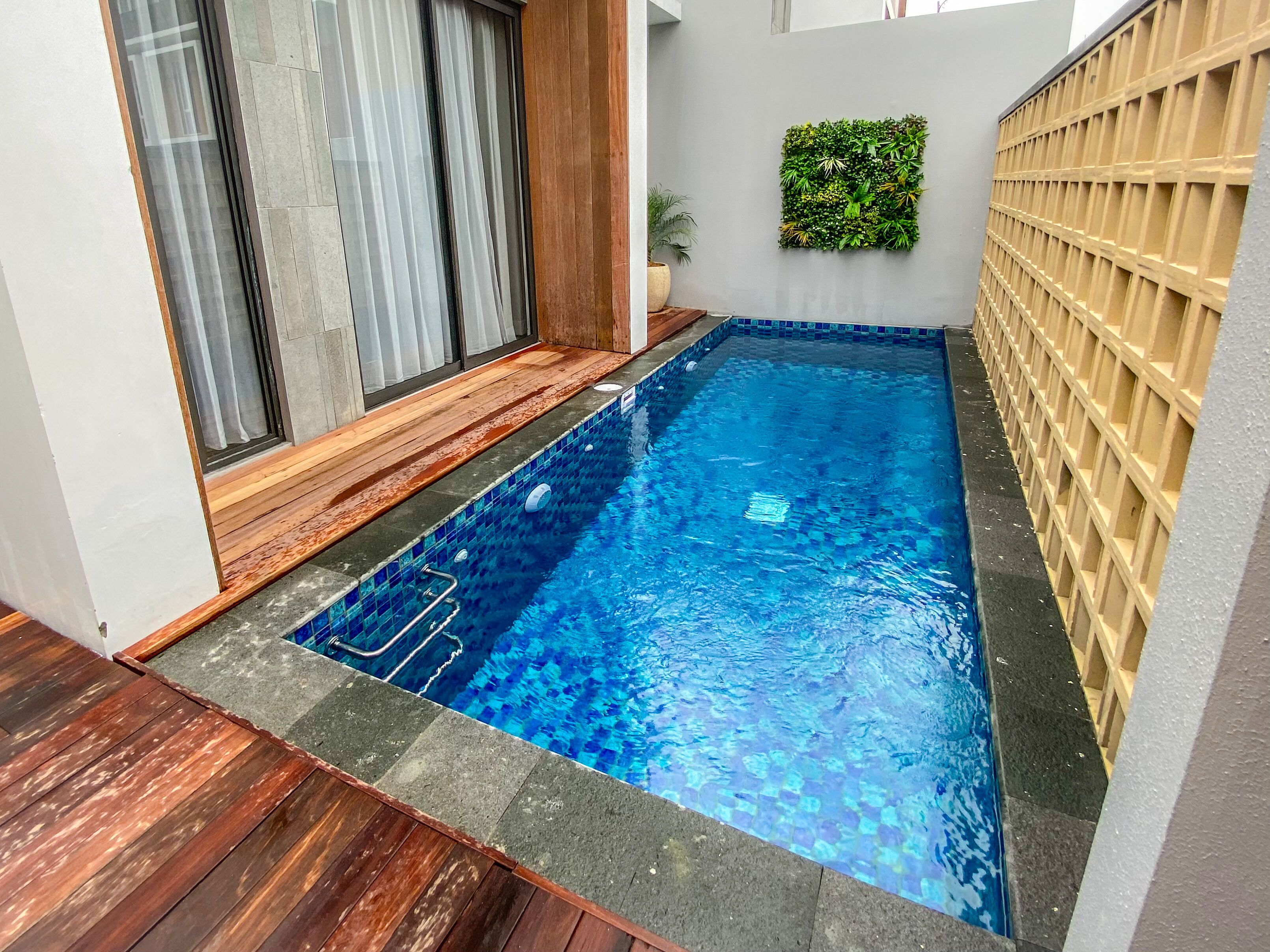 A rectangular swimming pool with a tiled edge, surrounded by wooden decking and a concrete border.