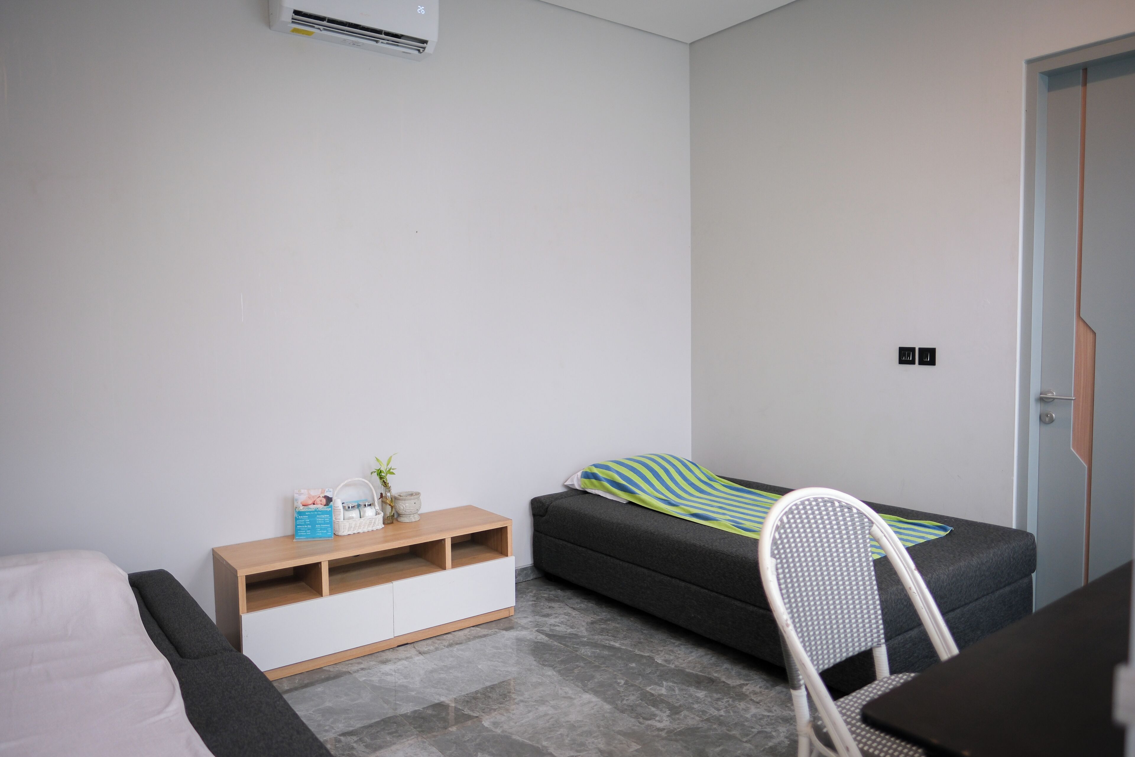 A modern, compact room with a grey sofa, a wooden side table, a white chair, and a small desk.