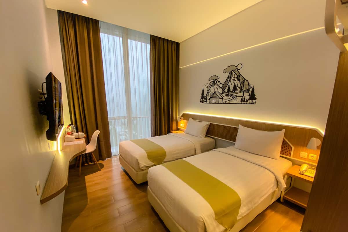 A hotel room with two beds, a desk, a chair, and a wall-mounted TV.