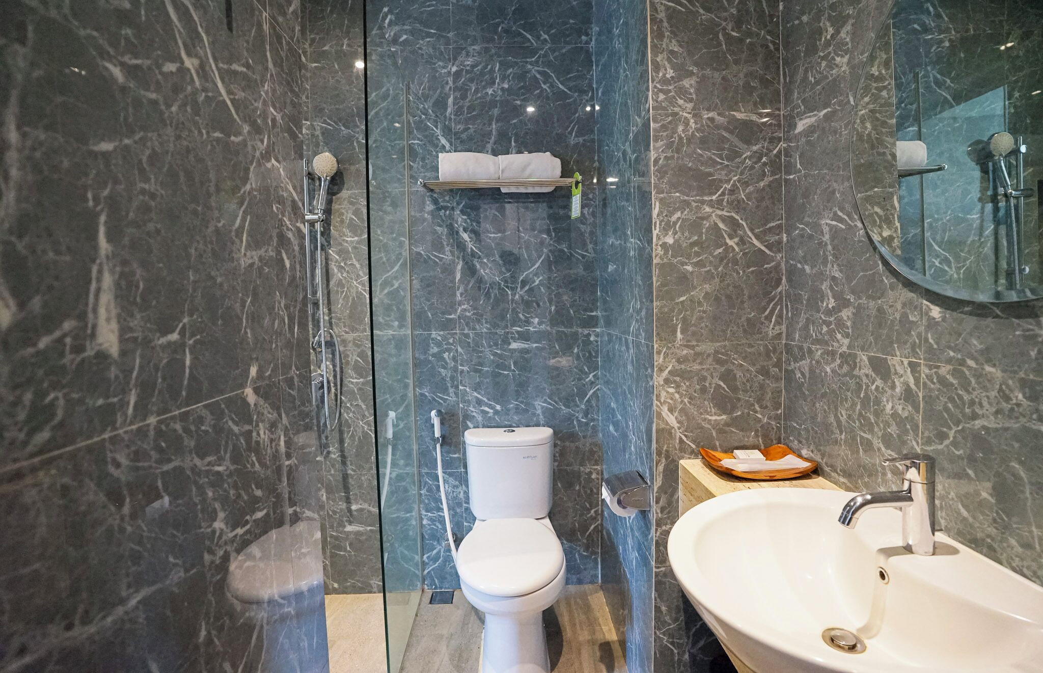 A modern bathroom with a marble wall, a toilet, a sink, and a glass shower enclosure.