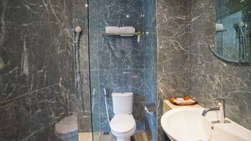 A modern bathroom with a marble wall, a toilet, a sink, and a glass shower enclosure.