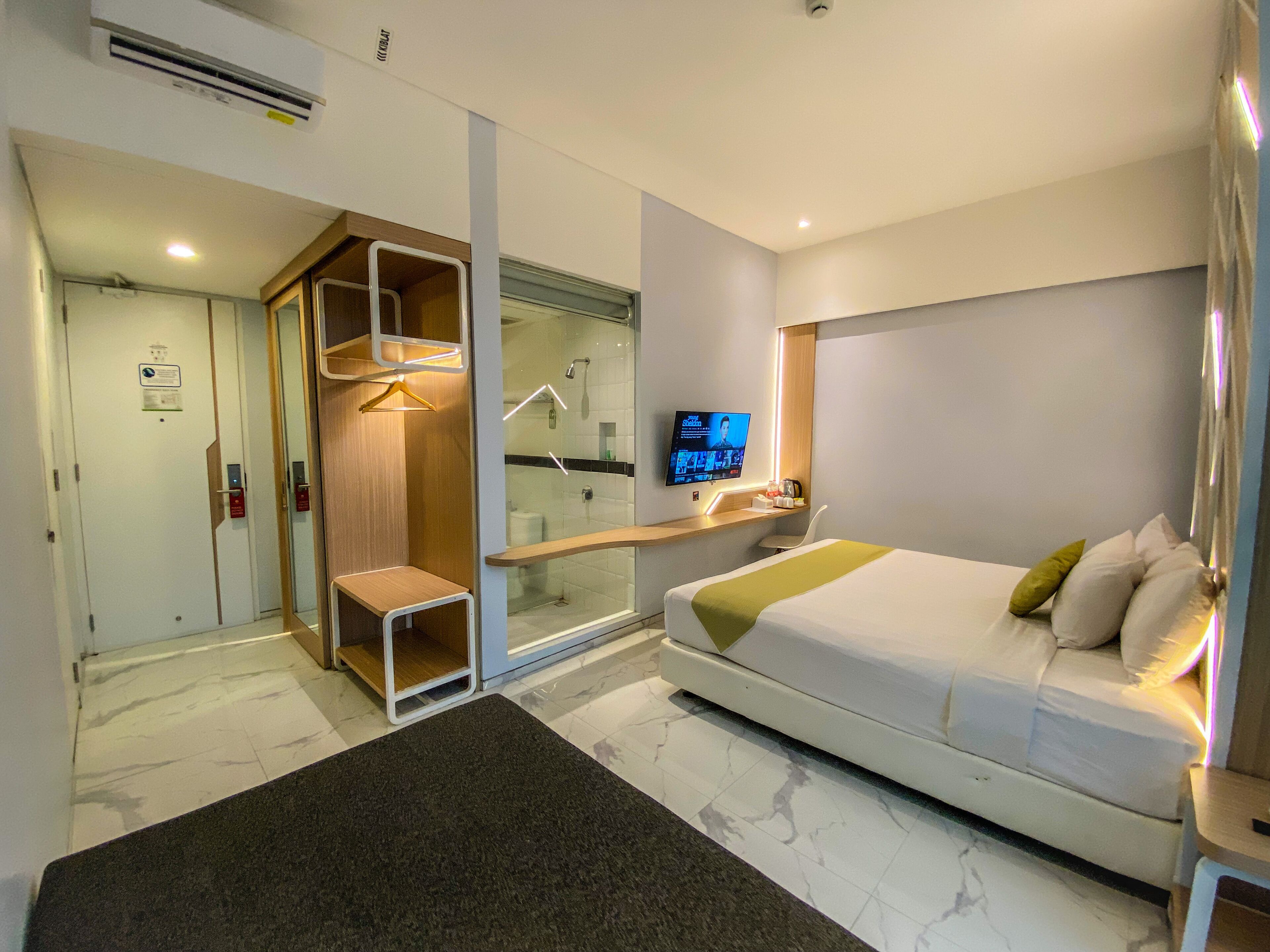 A modern hotel room with a bed, a TV, a shower, and a small seating area.