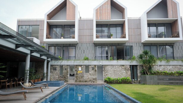 A modern building with a swimming pool, outdoor seating, and a stone facade. - Facade Hotel by Azana (Tawangmangu)