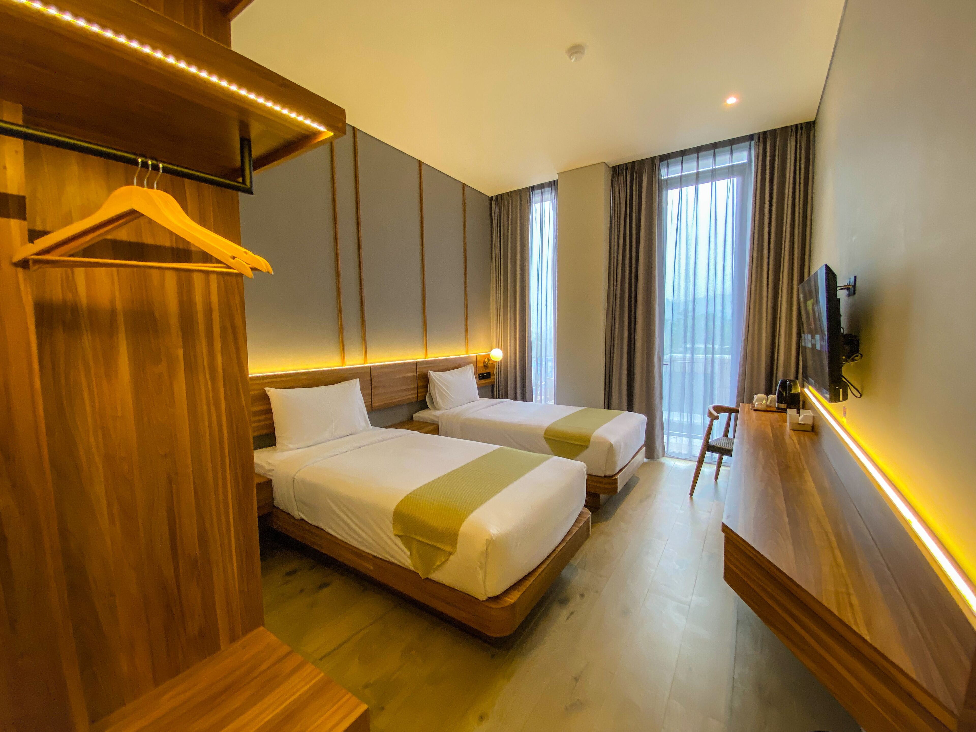 A hotel room with two beds, a TV, a desk, and a hanging coat rack.