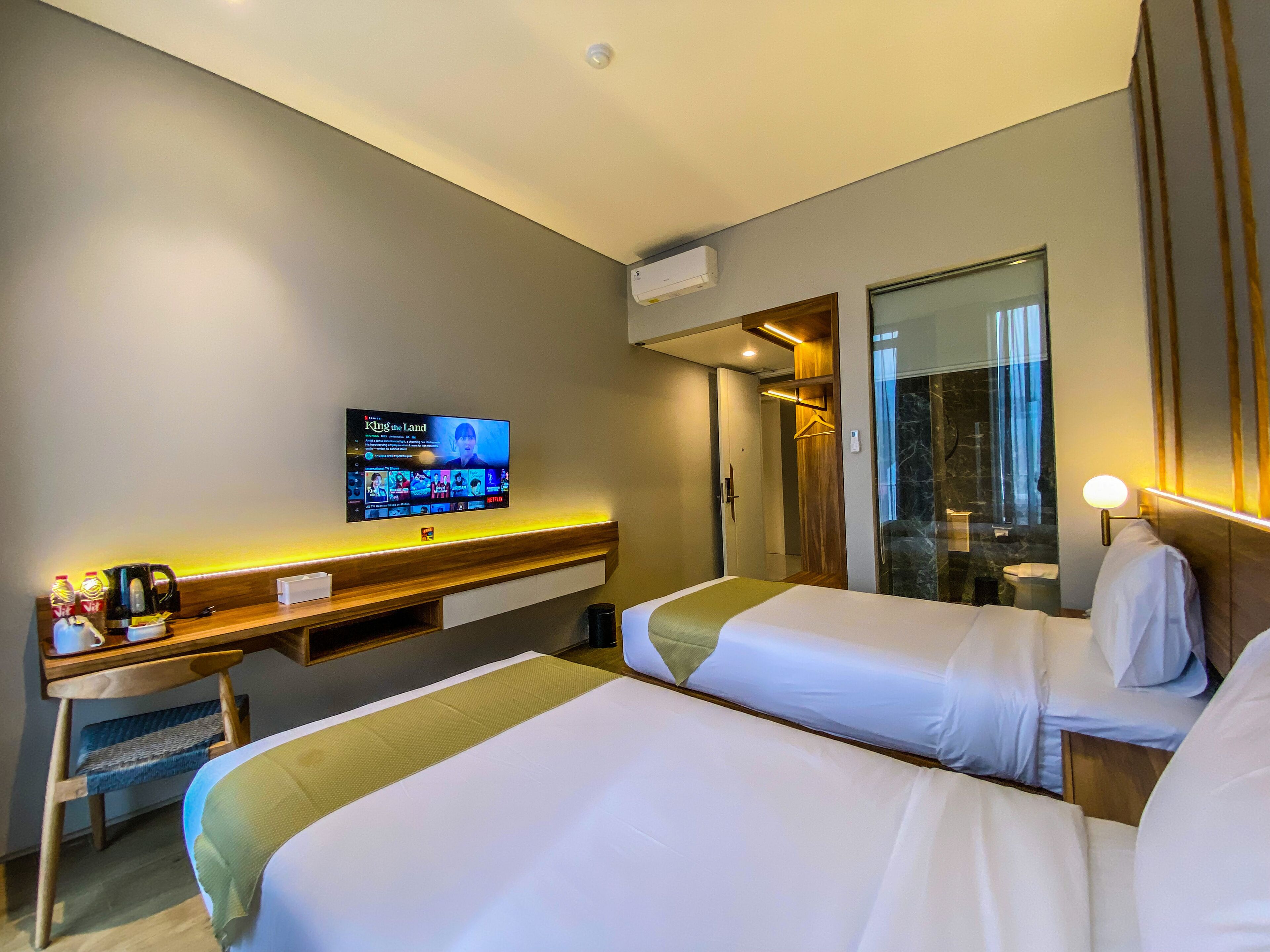 A hotel room with two beds, a desk with a coffee maker, a TV displaying 'King & i', and a mirror.