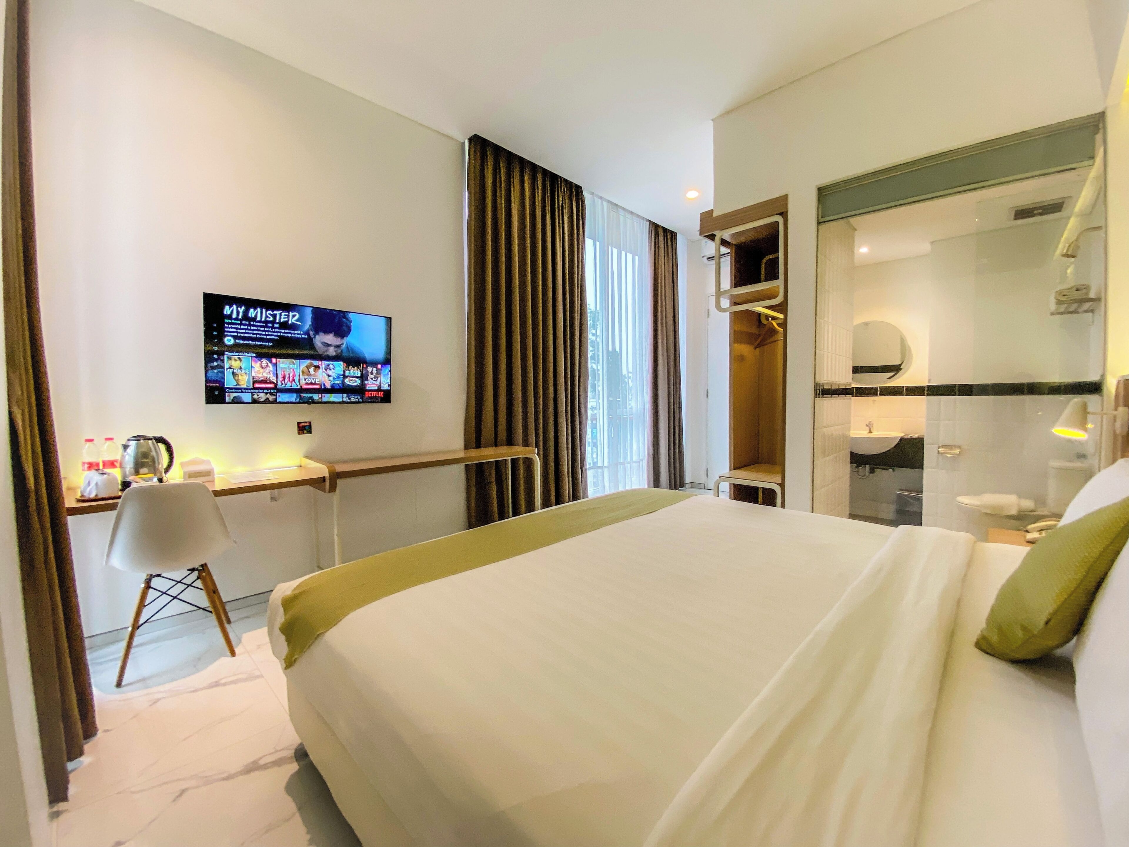 A hotel room with a bed, a desk, a TV, a shower, and a bathroom.