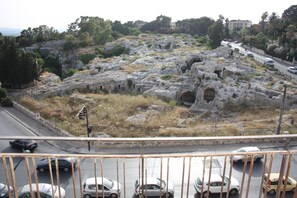 A view of ancient ruins with a road in the foreground. - Interno 10 (Syracuse)