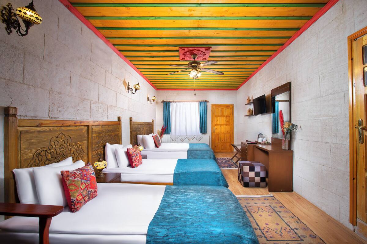A hotel room with three beds, a wooden ceiling, a television, and a wooden desk.