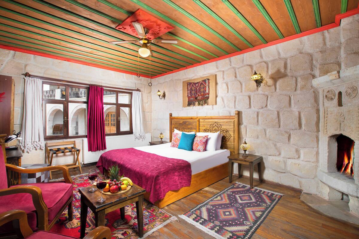 A cozy room with a bed, wooden furniture, a stone wall, a fireplace, and a ceiling fan.