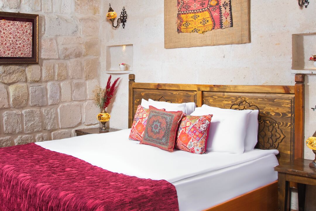 Una cama con cabecera de madera, ropa de cama blanca y almohadas de colores.