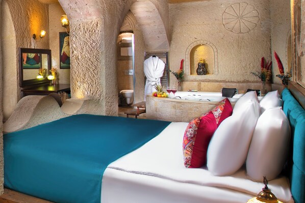 A spacious room with a large bed, a bathtub, and a stone wall. - Garden Inn Cappadocia (Avanos)