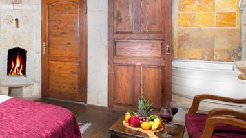 A hotel room with a fireplace, a wooden door, a fruit and wine display, and a red upholstered chair.