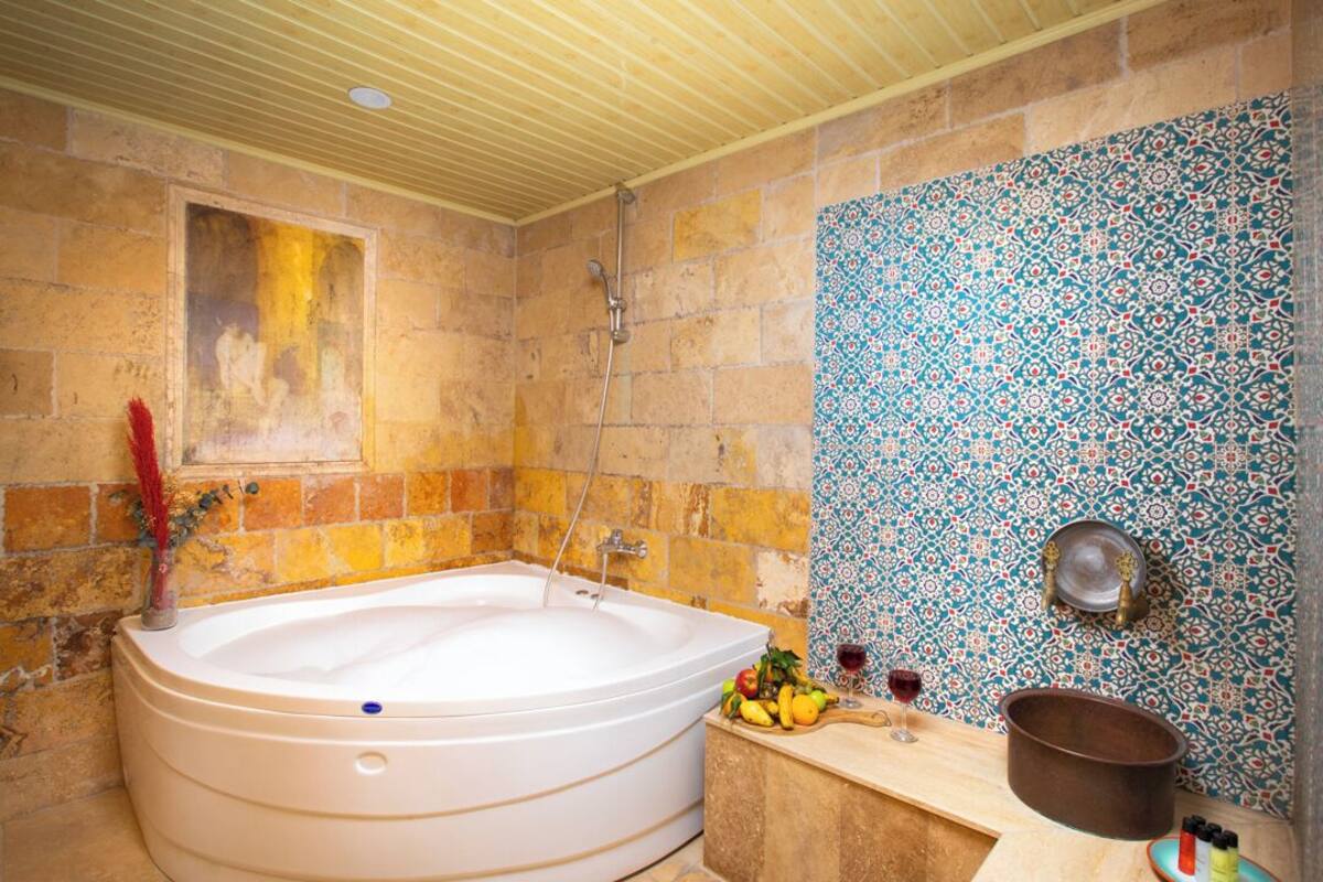 A bathroom with a large bathtub, a shower, and a sink with a decorative bowl. There are fruits and a wine glass on the counter.