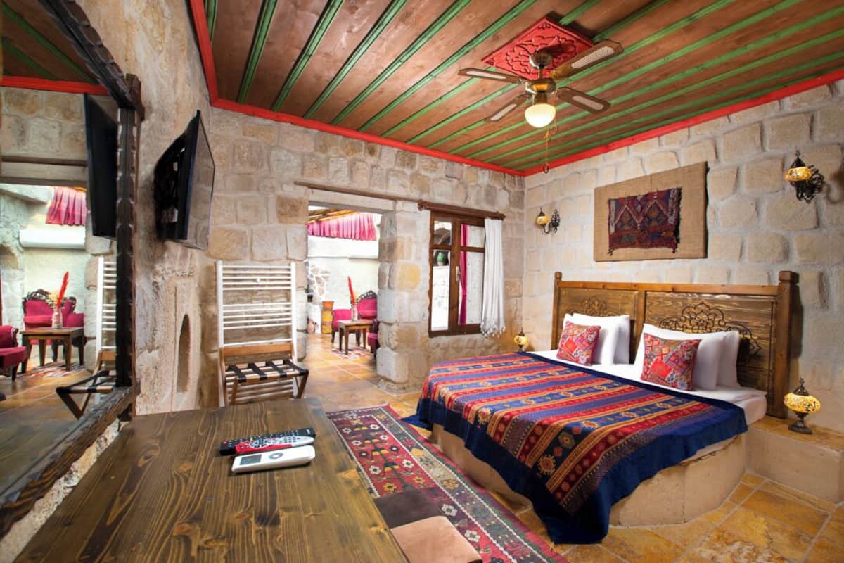 A cozy room with a stone wall, wooden ceiling, and a bed with colorful bedding.