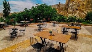 An outdoor café with tables and chairs, surrounded by greenery and a rocky landscape.