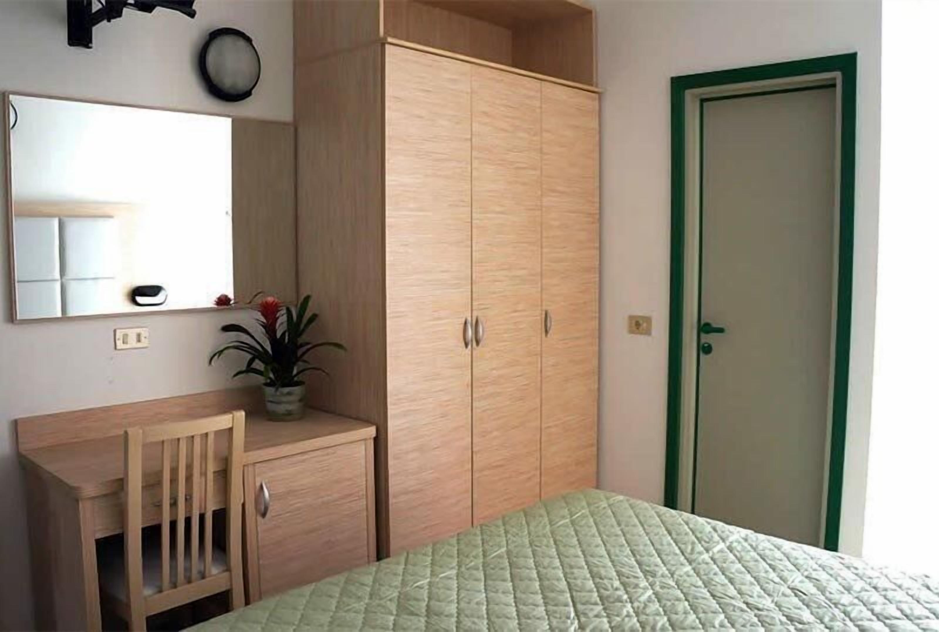 Un dormitorio con una cama, un armario de madera, un escritorio pequeño, un espejo y una puerta.