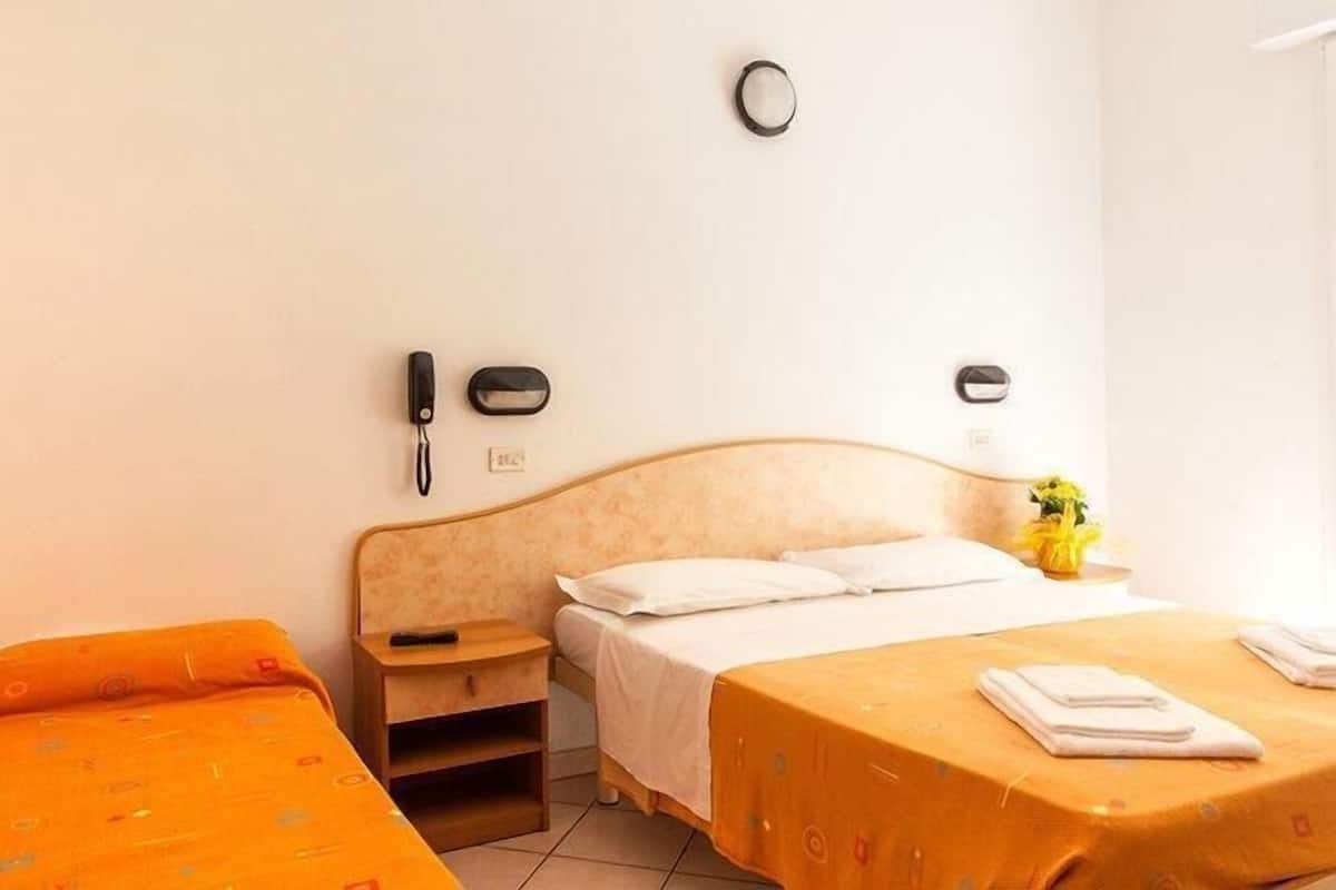 A hotel room with a bed, a bedside table, a nightstand, and a wall-mounted phone.