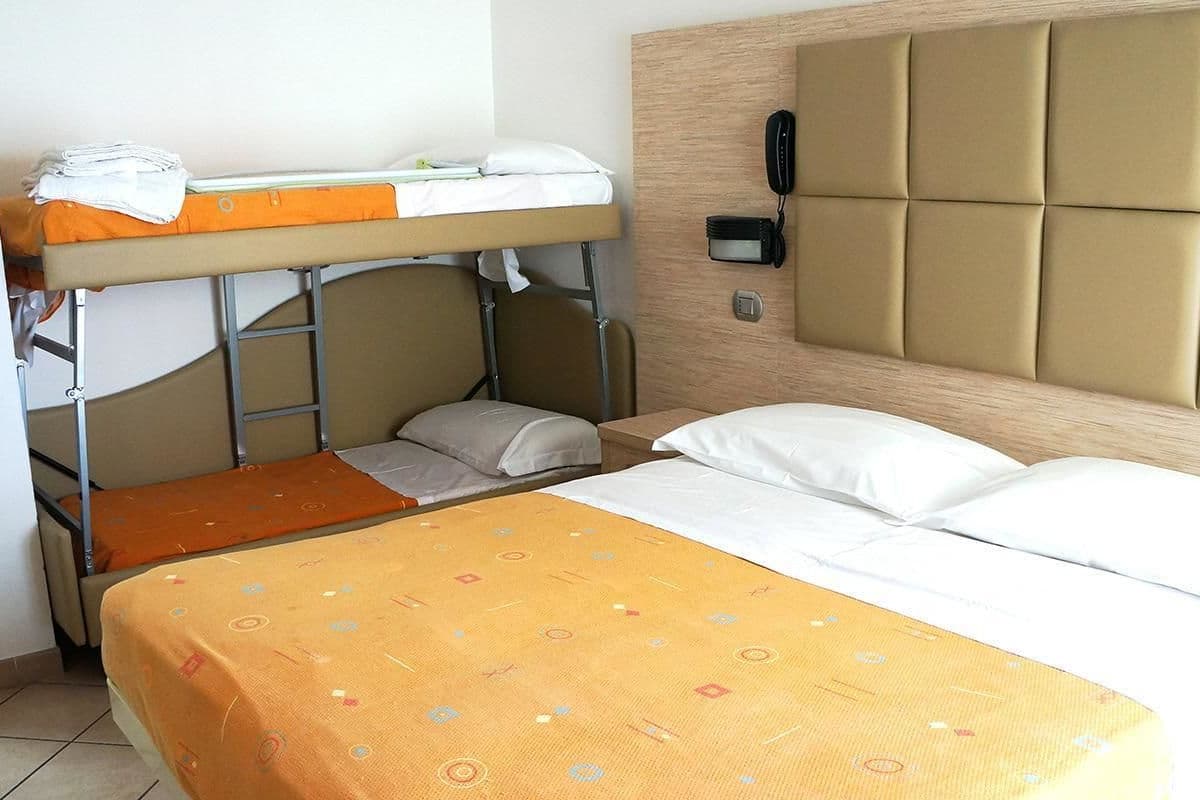 A hotel room with a bunk bed, a single bed, a telephone, and a wall-mounted light.