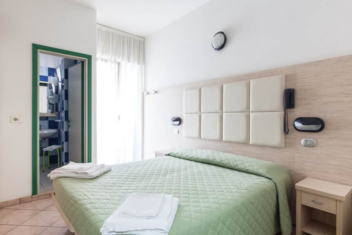 A hotel room with a bed, bedside table, and a mirror.