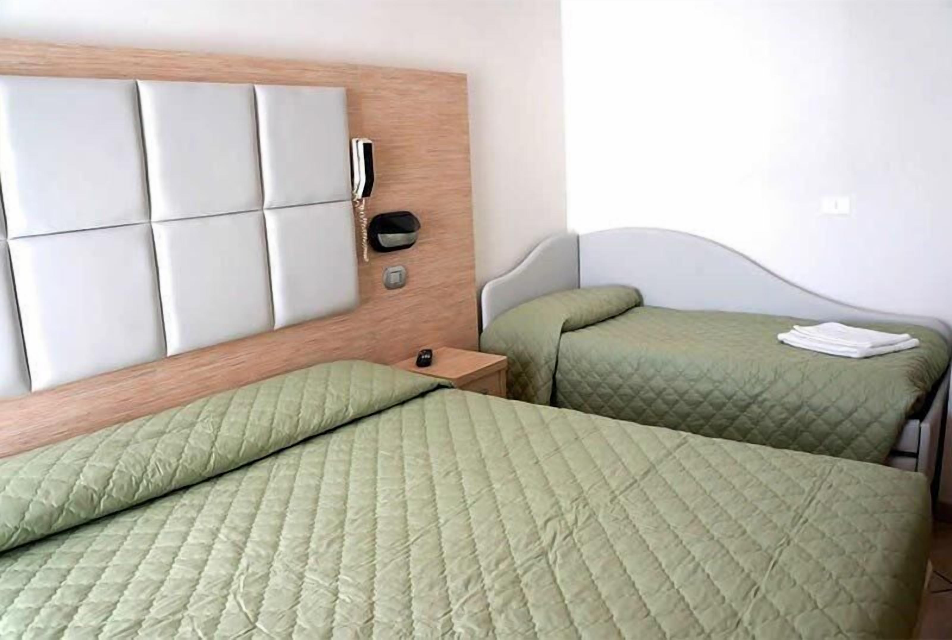 Ein Hotelzimmer mit zwei Betten, einem Holzkopfteil, einem Nachttischtelefon und einem kleinen Beistelltisch.