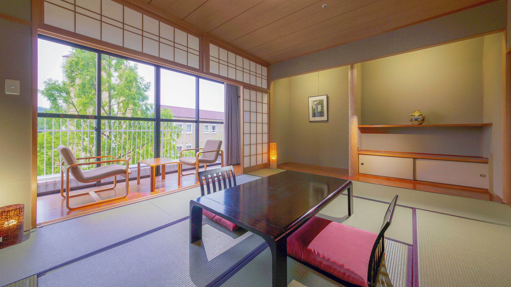 Una habitación japonesa tradicional con suelo de tatami, una mesa baja y una puerta corredera que da a un balcón con vistas a árboles y edificios.