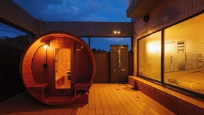 A wooden sauna structure with a bench inside, a shower area, and a glass wall with a view. - Shionomaru (Imabari)