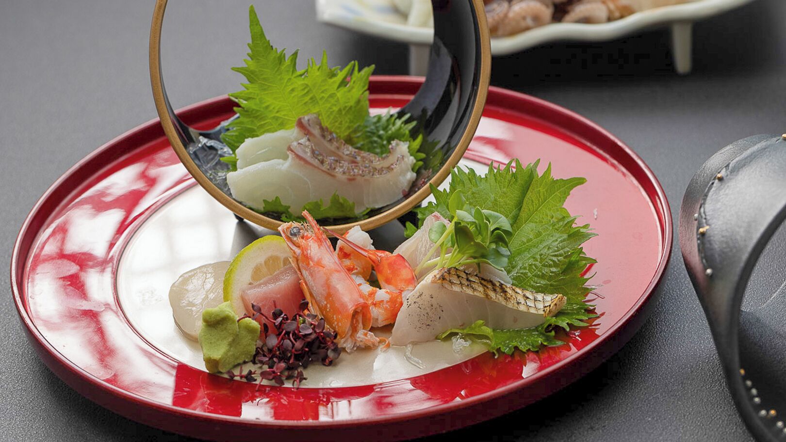 A seafood dish with a red plate, garnished with green leaves and a lemon slice.