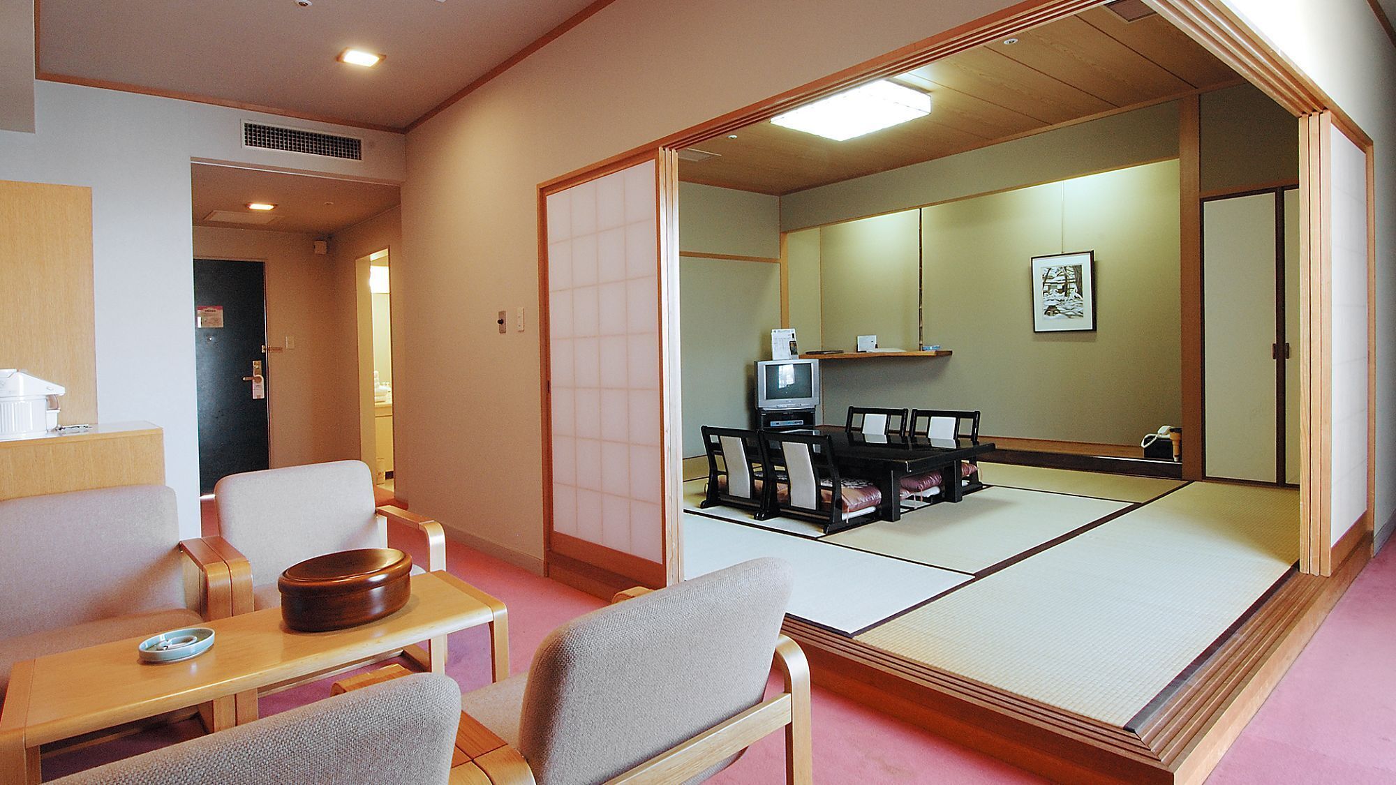 Een traditionele Japanse kamer met tatami vloerbedekking, een televisie en een kleine tafel met stoelen.
