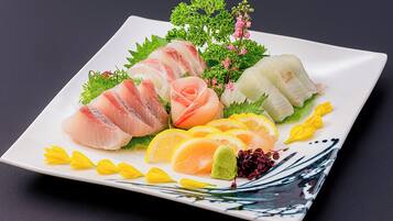 A square plate with various sashimi pieces, garnishes, and decorative elements.