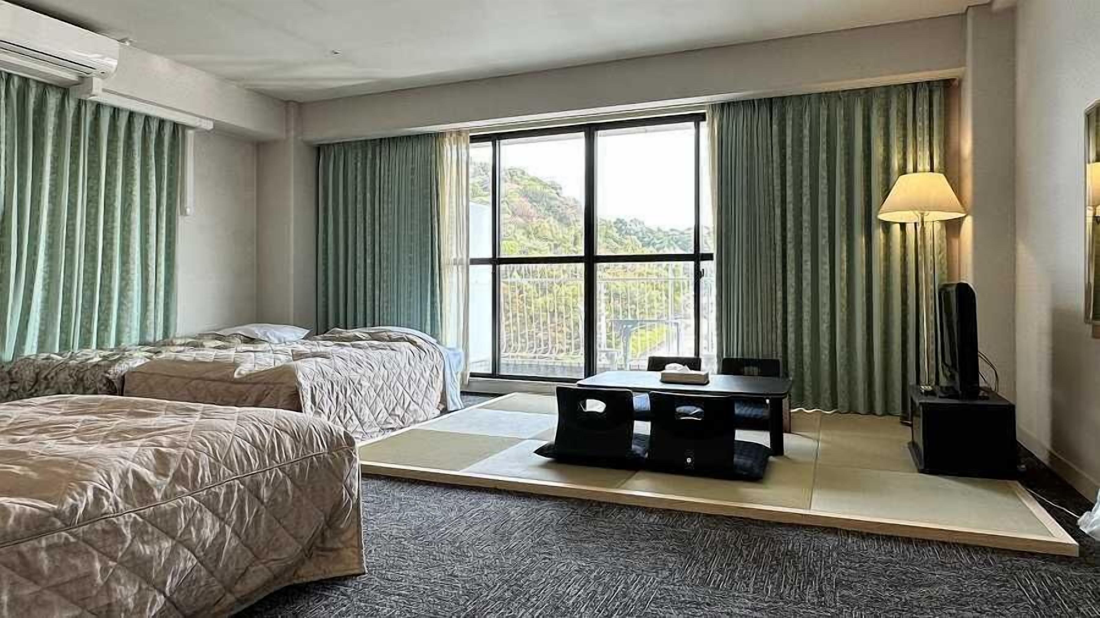 Een hotelkamer met twee bedden, een tafeltje, een televisie en een raam met gordijnen.