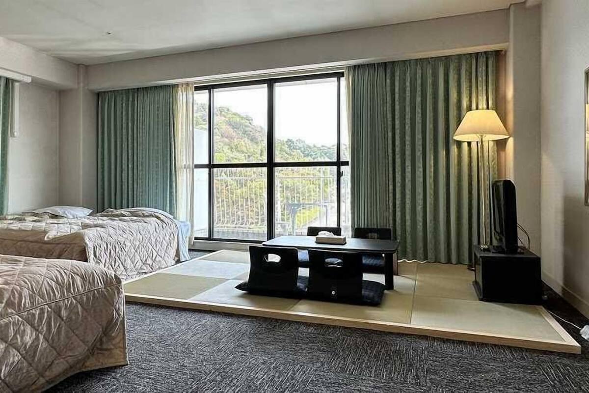 A hotel room with two beds, a small table, a TV, and a window with curtains.