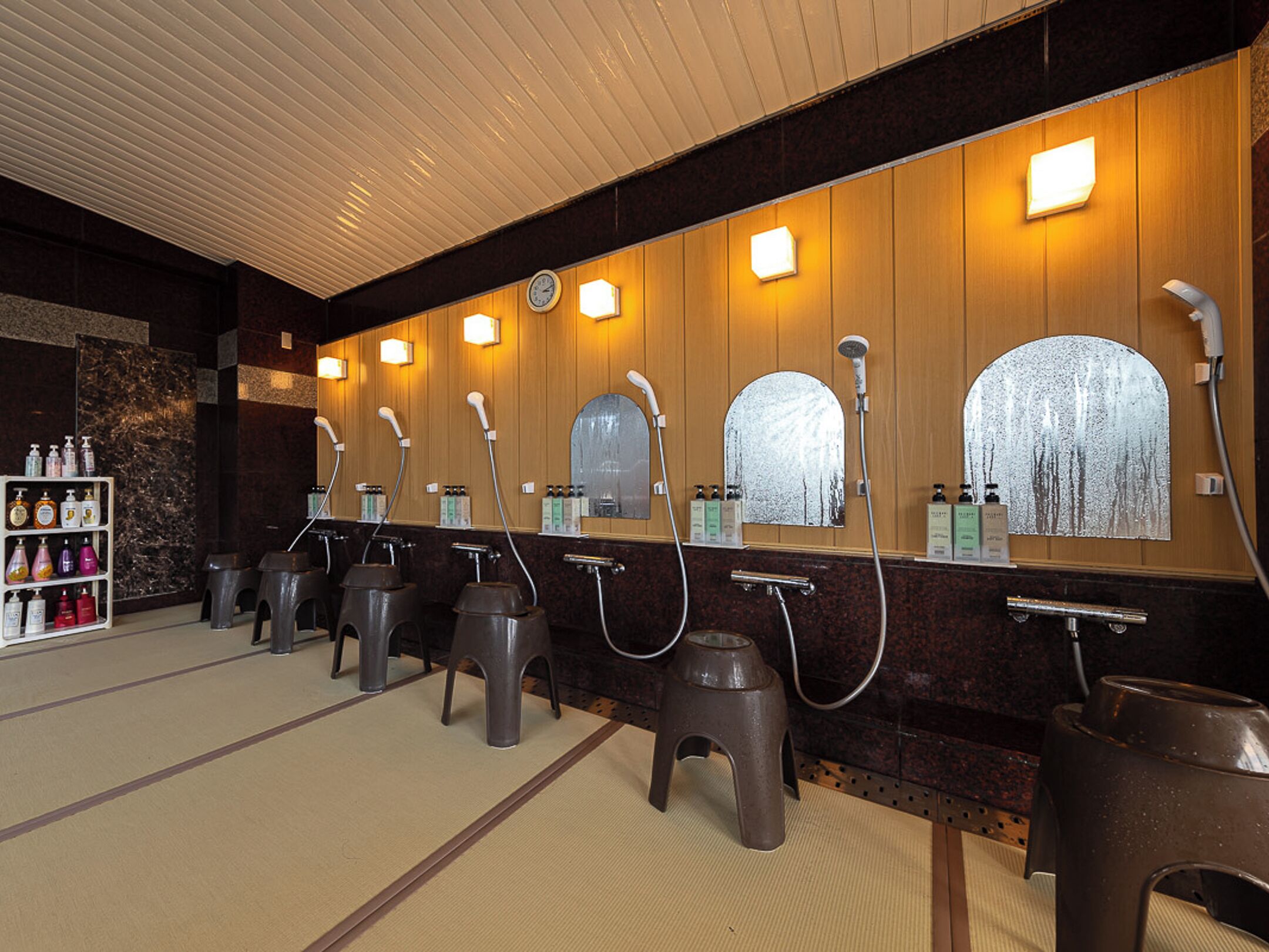 Baño público con varios lavamanos, espejos y un estante con artículos de aseo.