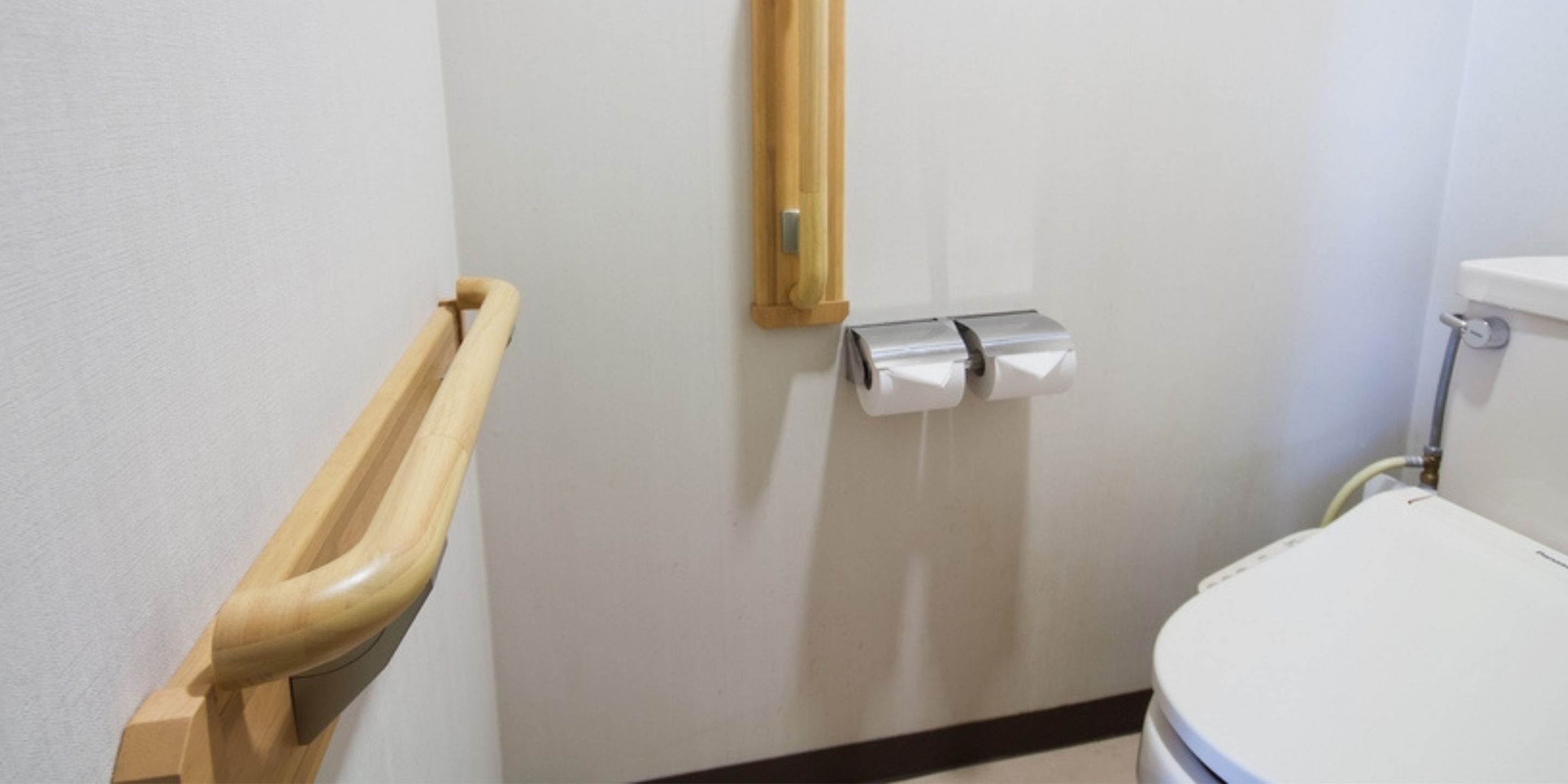 Baño con inodoro, barra de apoyo y dispensador de toallas de papel.