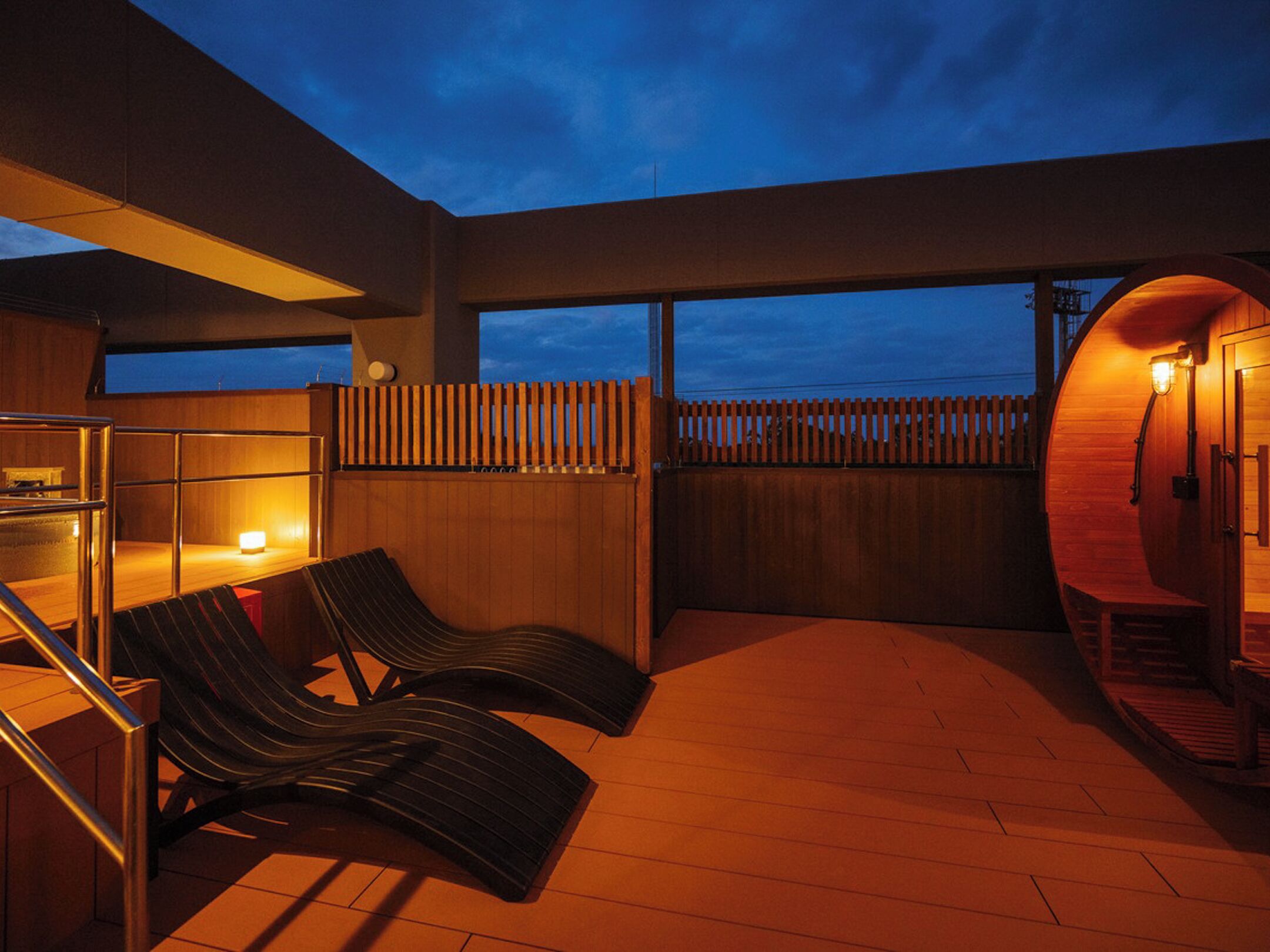 Un área de descanso al aire libre con un deck de madera, dos sillones, una mesita y una valla de madera.