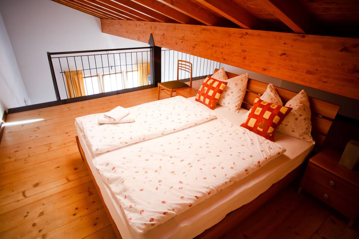 Un dormitorio con techo de madera, una cama con ropa de cama floral, una silla y una mesita de noche.