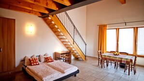 A bedroom with a bed, a desk, a chair, a dining table with chairs, and a staircase. - Agriturismo La Molinalda (Castelnuovo del Garda)