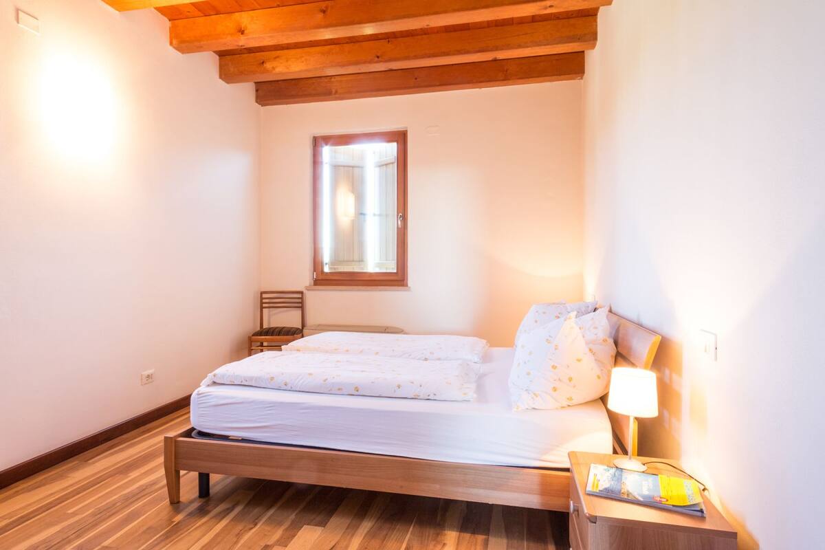 Un dormitorio pequeño y acogedor con una cama de madera, una mesita de noche con una lámpara y una ventana con vistas.
