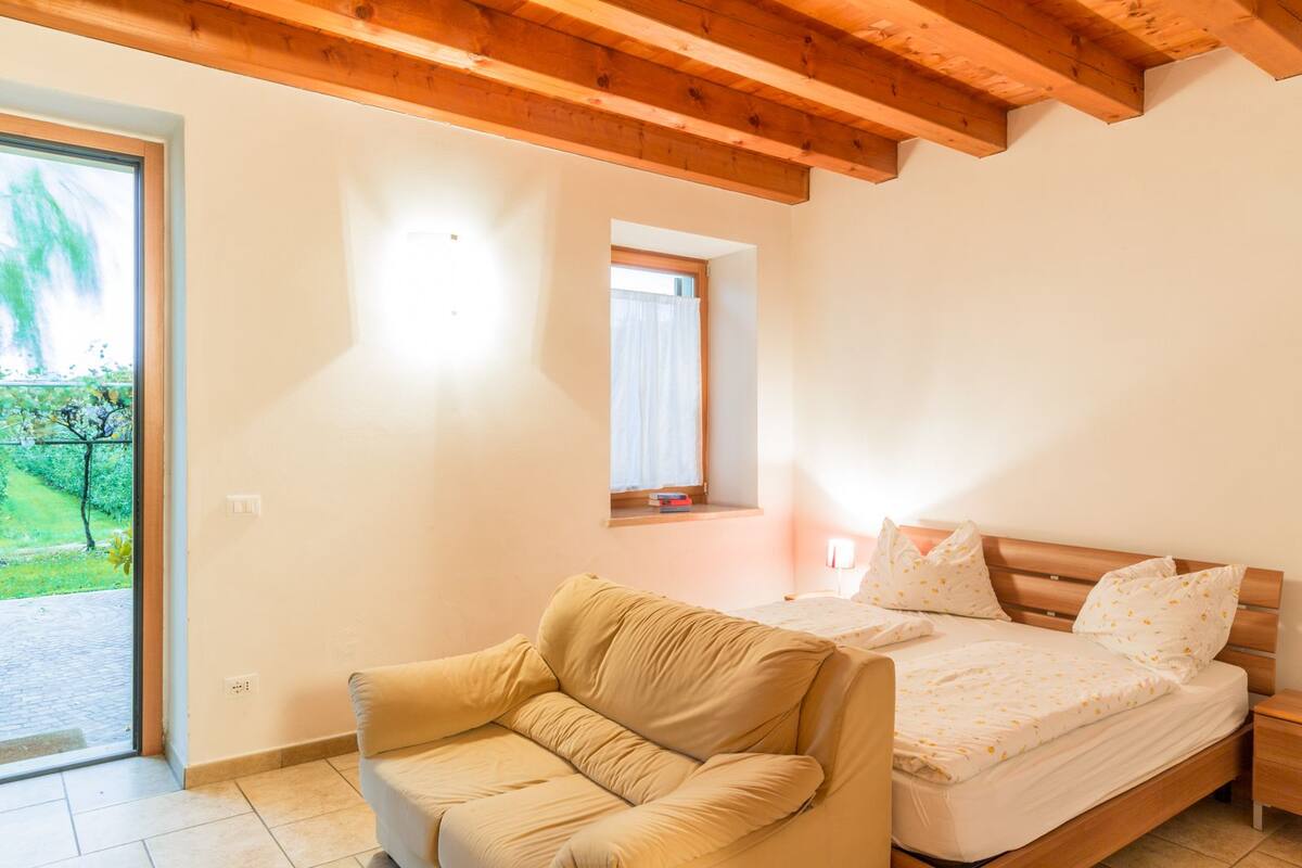 Un dormitorio con una cama, un sofá, una ventana y una puerta que da a un jardín.